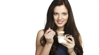 Young female enjoying taste of yogurt isolated on white