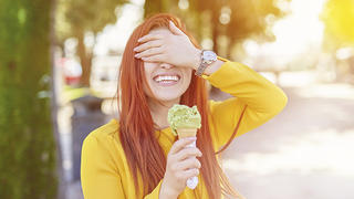 happy woman outdoors playing with her icecream and covering face, big toothy smile.