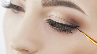 Close up of female eyes. The young woman is applying the eyeliner on her eye