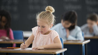 A multi-ethnic group of elementary age children are sitting together in class and are working on a writing assignment.