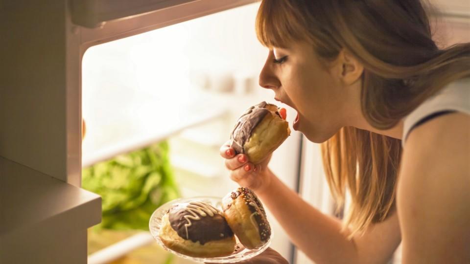 Junge Frau isst Schokokuchen am Kühlschrank