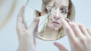 Insecure pretty young woman holding broken mirror