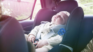 Little boys has fallen asleep during a road trip. He sit securely in a baby car seat and wears a seat belt.