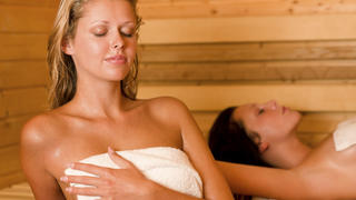 Sauna two healthy beautiful women relaxing sweating lying covered towels