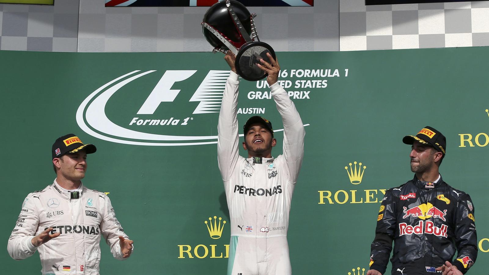 Formula One F1 - U.S. Grand Prix - Circuit of the Americas, Austin, Texas, U.S., 23/10/16. Mercedes' Lewis Hamilton of Britain raises his victory trophy as second placed finisher and teammate Nico Rosberg of Germany (L) and third placed Red Bull's Da