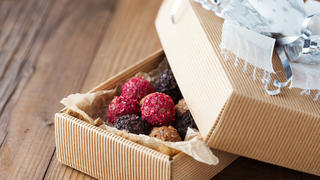 Assorted dark chocolate truffles with dried strawberry pieces and chopped hazelnuts on rustic wooden background, selective focus. Christmas time