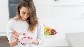 Beautiful young woman eating a healthy breakfast at home and smiling