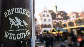 Ein Aufkleber mit der Aufschrift "Refugees welcome" hängt am 05.12.2016 in der Innenstadt von Freiburg (Baden-Württemberg) am Rathausplatz an einem Masten. Ein unbegleiteter minderjähriger Flüchtling wird verdächtigt, in Freiburg eine 19 Jahre alte Studentin umgebracht zu haben. Die Tat hat eine große politische Diskussion ausgelöst. Foto: Patrick Seeger/dpa +++(c) dpa - Bildfunk+++