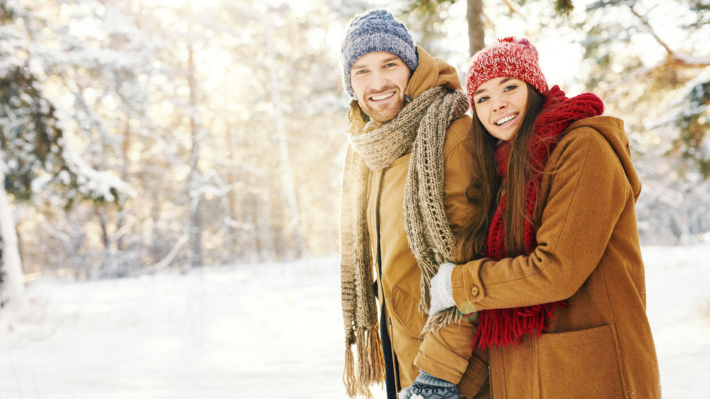 Ein glückliches Pärchen, eingepackt in wintertauglicher Kleidung, bei einem Winterspaziergang im Schnee.