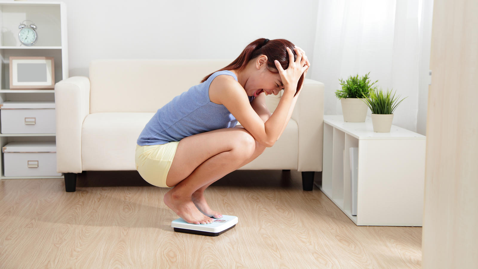 Upset woman on weigh scale at home.