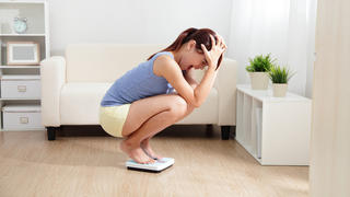 Upset woman on weigh scale at home, asian