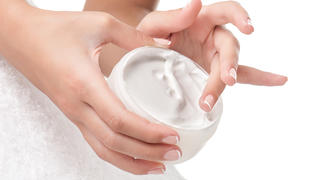 Woman applying body cream. Close-up composition of hands with white jar isolated on white background. Horizontal composition.