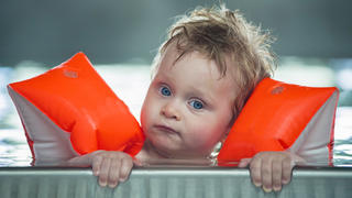 Baby boy makes face in a swiming pool.  DOF focus on babys and mother face with  defocused background.