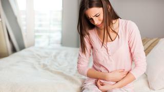 Young woman with a stomach ache in the bedroom, sitting holding her abdomen