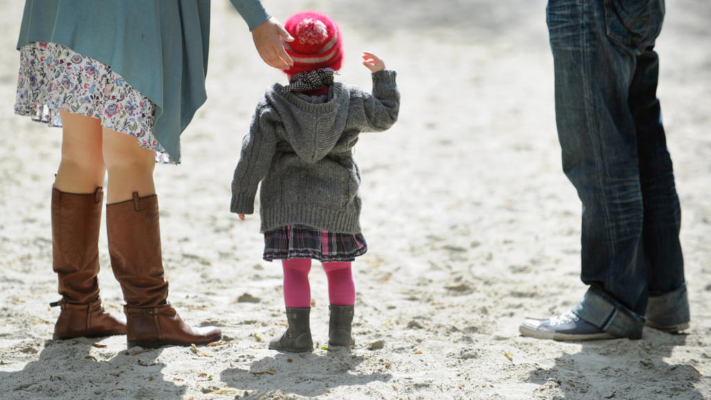 ARCHIV - Ein Kind steht am 16.04.2011 zwischen seinen Eltern auf einem Spielplatz in München (Bayern). (zu dpa "BGH lässt abwechselnde Kinderbetreuung nach Trennung prinzipiell zu" am 27.02.2017) Foto: Andreas Gebert/dpa +++(c) dpa - Bildfunk+++