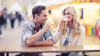A young happy couple is sitting at a table and drinking beer during the traditional festival on the Alexanderplatz (Eastern Berlin, Germany) late in the evening.