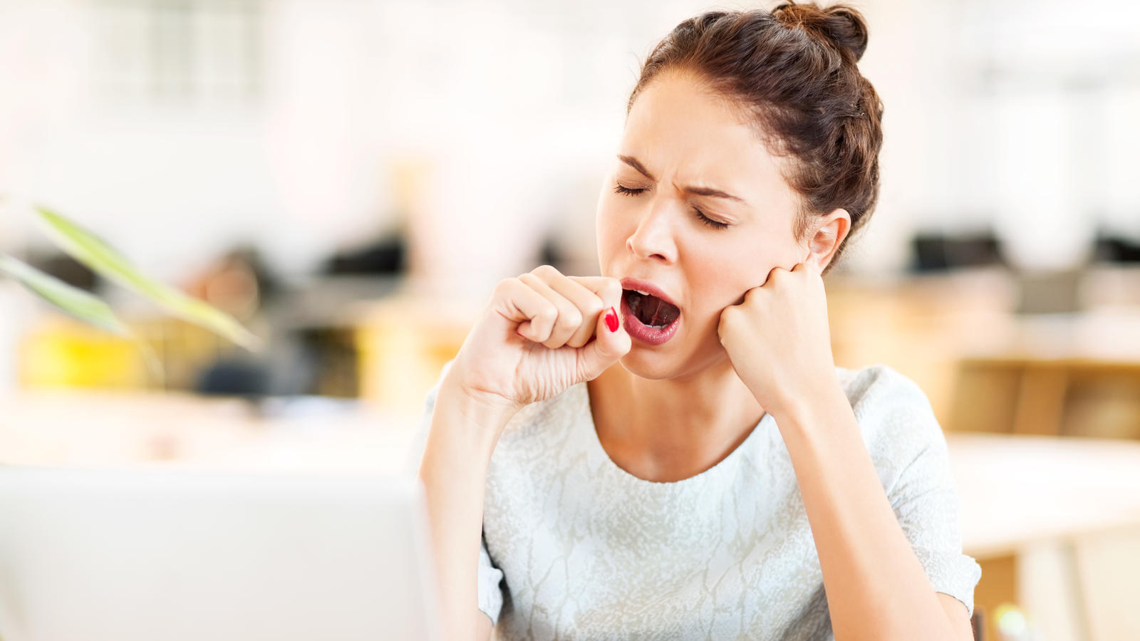 Tired female entrepreneur yawning in office. Horizontal shot.