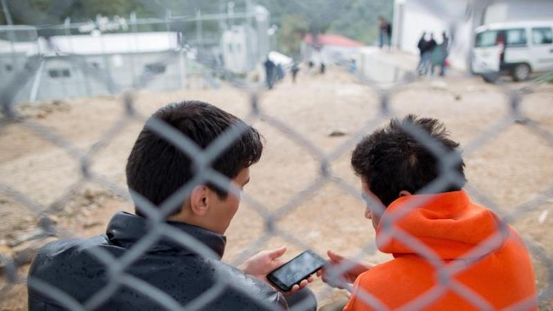 Flüchtlinge sitzen in dem Flüchtlingscamp Moria auf der griechischen Insel Lesbos hinter einem Zaun. Moria gilt als einer der größten Flüchtlings-Hotospots in Griechenland.