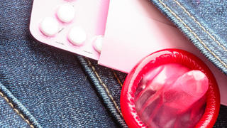 Healthcare medicine, contraception and birth control. Closeup oral contraceptive pills, red condom on denim pocket background