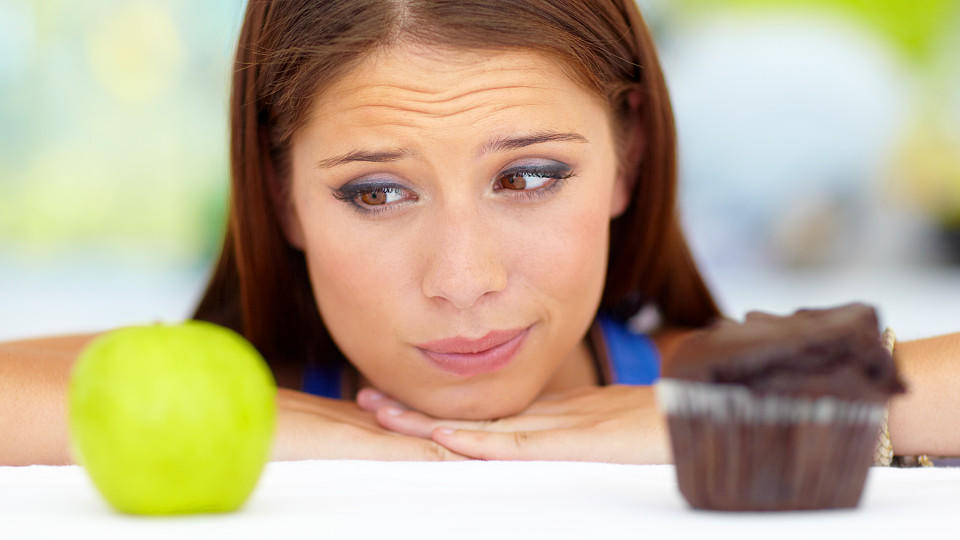 Wistful young woman trying to choose between unhealthy and healthy food options