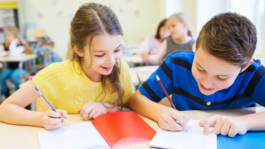 education, elementary school, learning and people concept - group of school kids with pens and notebooks writing test in classroom