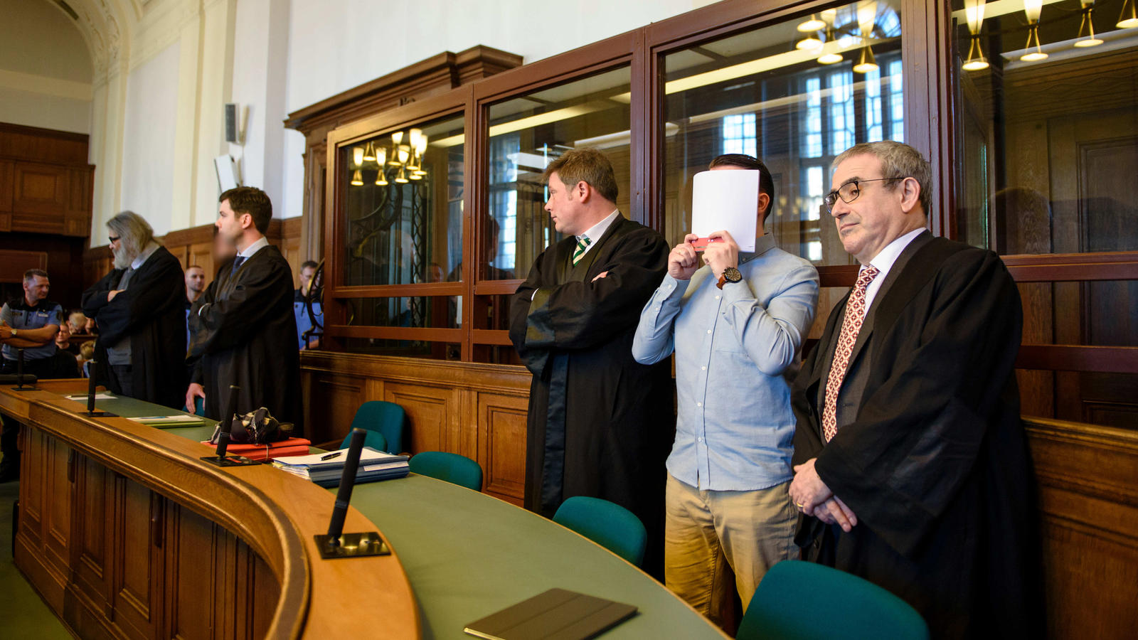Die Angeklagte Hamdi H. (2.v.r) und  Marvin N. (5.v.r, hzalb verdeckt)  stehen am 27.02.2017 in Berlin in einem Gerichtssaal des Landgerichtes Berlin zwischen ihren Anwälten, Hamdi H. hält sich eine Akte vor das Gesicht. 