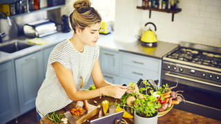High angle view of young woman plucking mint leaves. Female is wearing casuals in kitchen. She is preparing food from recipe on tablet at kitchen island.