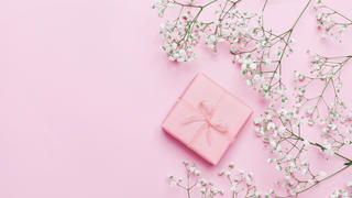 Gift or present box and flower on pink table from above. Pastel color. Greeting card. Flat lay style.