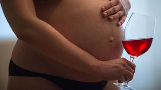 Eine nackte junge schwangere Frau hält ein Glas Wein in der rechten Hand, während die linke auf ihrem Bauch liegt. Foto: Hans Wiedl . Foto: Hans Wiedl  - Model Released
