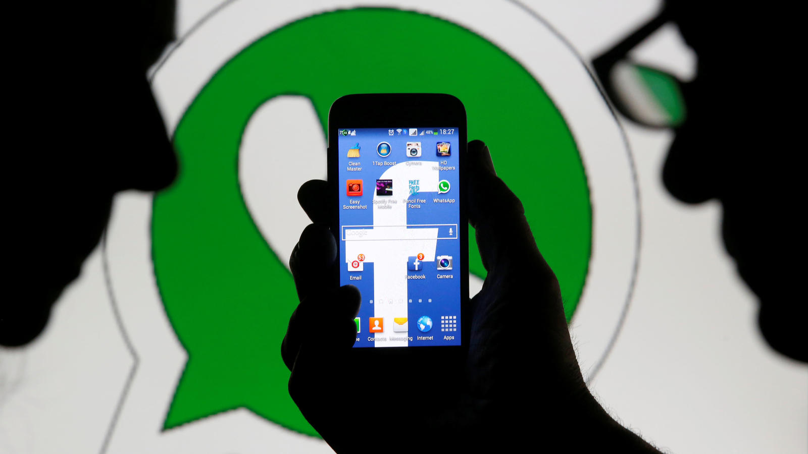FILE PHOTO: An illustration photo shows a man holding a smart phone with a Facebook logo as its screen wallpaper in front of a WhatsApp messenger logo February 20, 2014.   REUTERS/Dado Ruvic /Illustration/File Photo