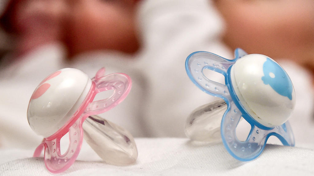 ARCHIV - Ein rosa und ein blauer Schnuller, aufgenommen am 14.04.2015 vor zwei Babys in Frankfurt (Oder) in Brandenburg. Die Geburtenrate in Deutschland ist so hoch wie seit mehr als 30 Jahren nicht mehr. Trotzdem bekommen die Frauen in vielen andere
