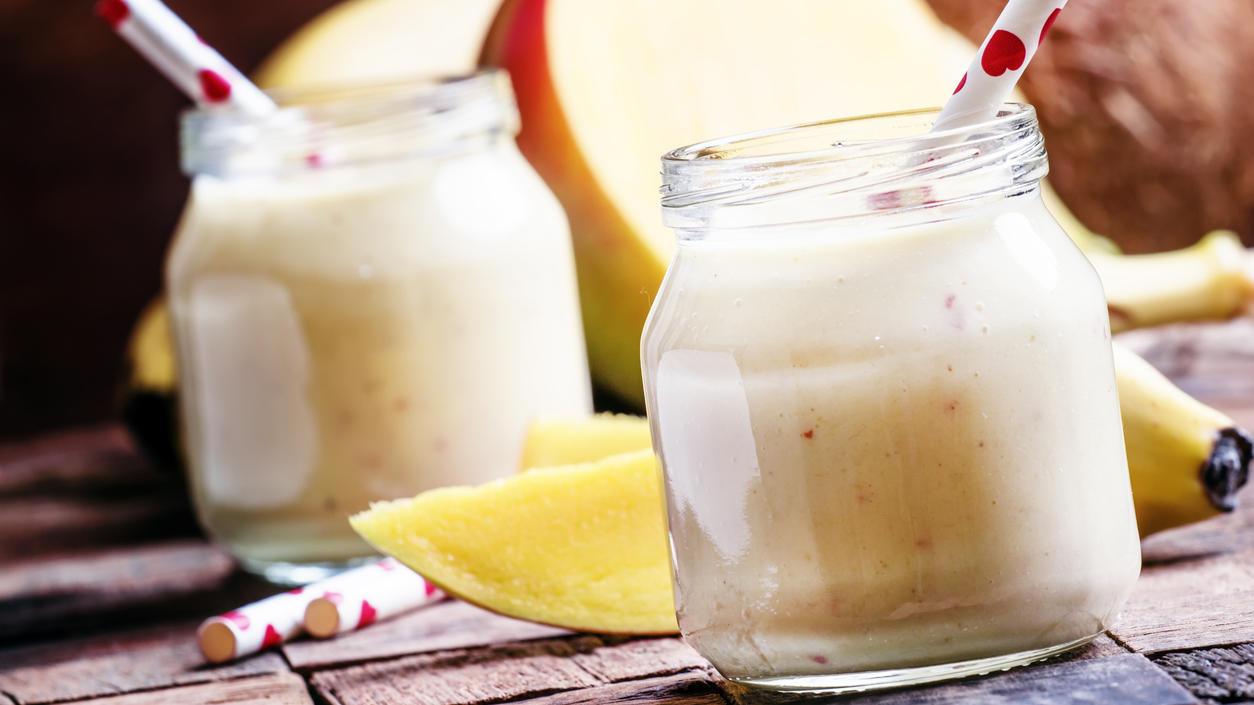 Banana mango smoothie with coconut in a glass jar, vintage wooden background, selective focus