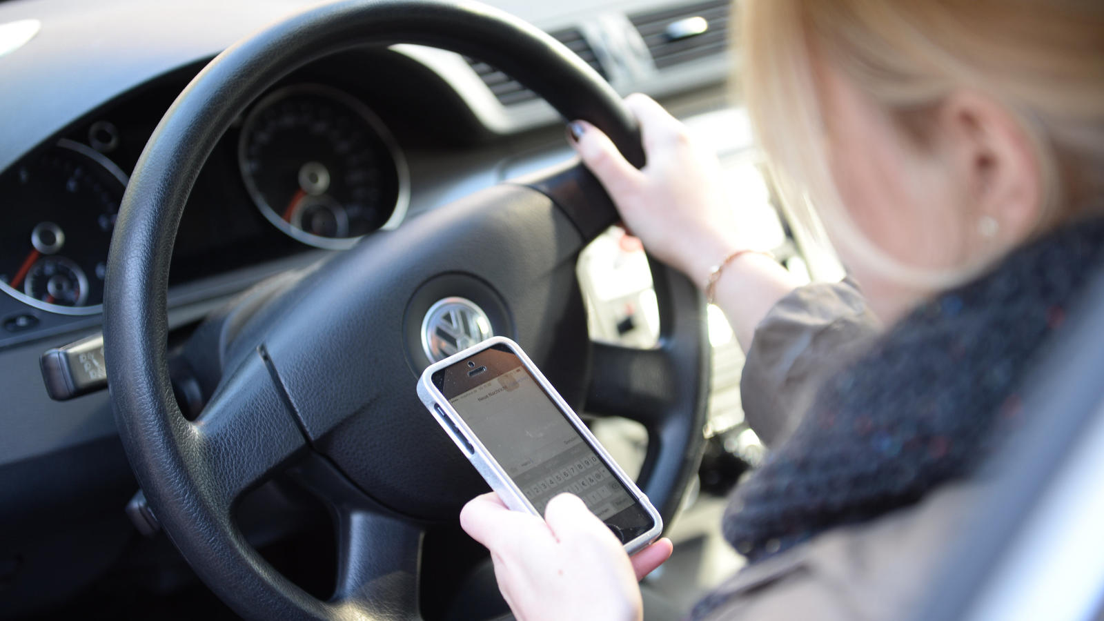 Eine Frau sitzt im Auto am Steuer und liest Nachrichten auf ihrem Smartphone.