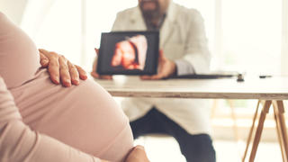 Pregnant woman looking at ultrasound image of her baby at doctor's office.