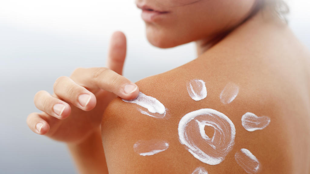 Frau cremt sich die Schulter mit Sonnencreme ein. Die Creme stellt eine Sonne dar.