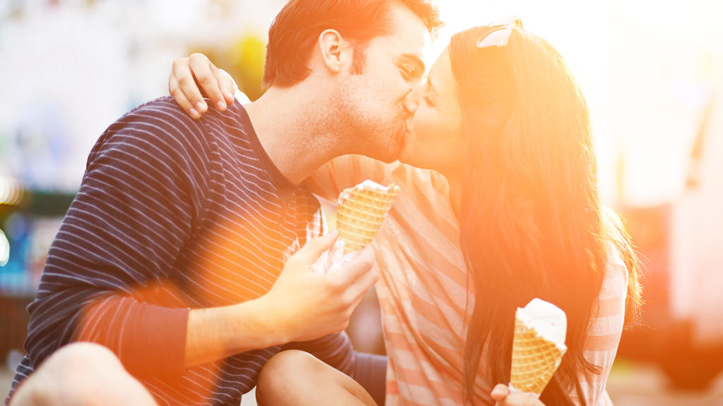 photo of a romantic couple kissing while holding ice cream