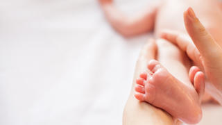 Mother makes massage for happy baby, apply oil on the foot, with white background