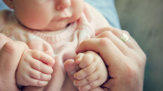 Focus on the hands of a 3 month old baby girl holding the fingers of her father.  Vintage style color filter.