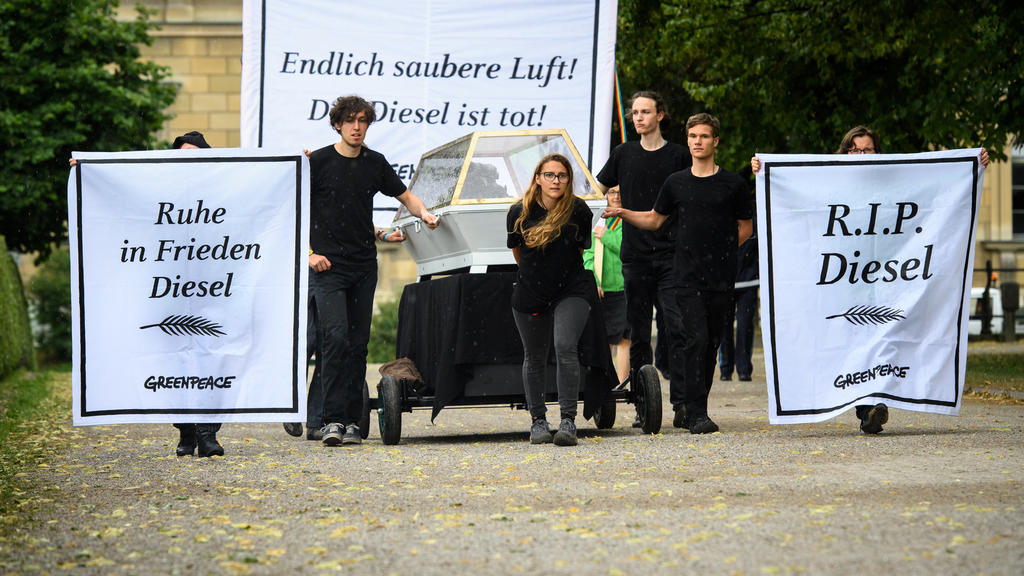 ARCHIV - Greenpeace-Aktivisten ziehen am 28.06.2017 während einer Aktion zum Diesel-Gipfel hinter der Staatskanzlei in München (Bayern) einen Sarg mit einem 1,6 Liter Diesel-Motor des Volkswagenkonzerns durch den Hofgarten. Dazu tragen sie Banner mit