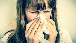 Young woman with allergy or flu cold symptoms sneezing in tissue