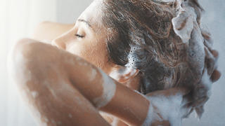 Closeup side view of mid 20's woman completely enjoying washiing her blond colored hair. She's going her finger through soapy hair, faced to the bathroom window.