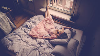 Portrait of a beautiful woman, resting on the bed by the window in a beautiful pink dress 