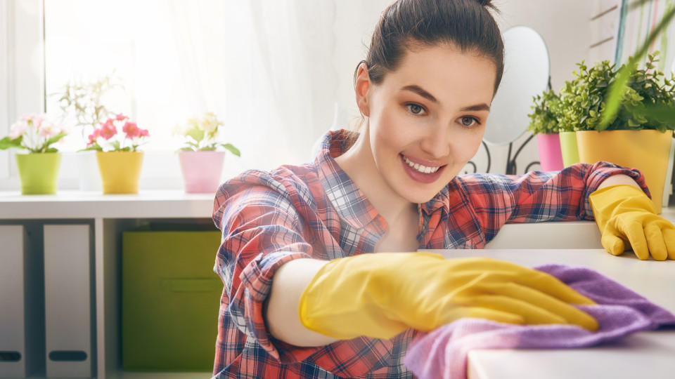 Junge Frau putzt ihre Küche mit Gummihandschuhen und einem Spültuch. 