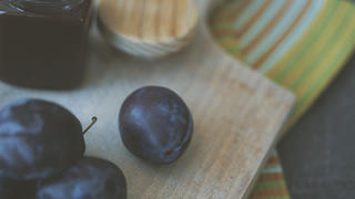 Close up of fresh plums and plum jam on cutting board, green napkins.