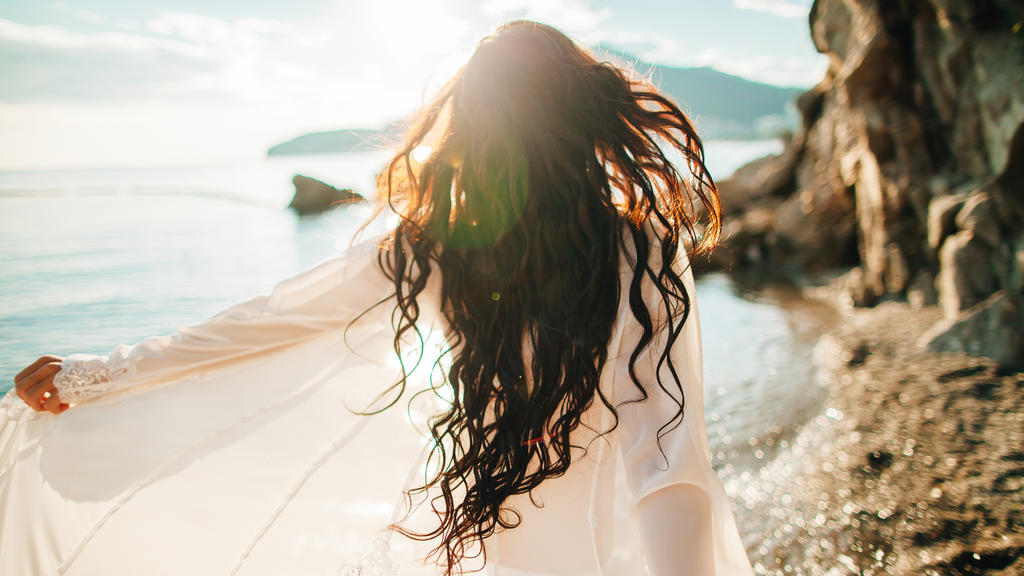 girl running dreamy with wind in hair and sunflare on beach sunset. defocus