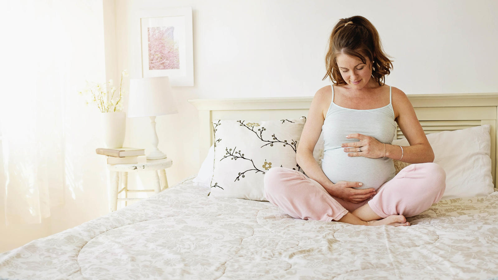 Smiling pregnant woman sitting on bed, Laechelnde schwangere Frau, die auf dem Bett sitzt | Verwendung weltweit, Keine Weitergabe an Wiederverkäufer.