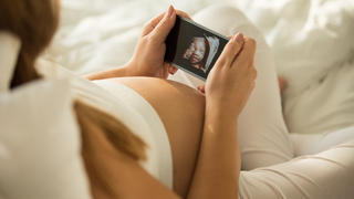 Pregnant mid adult woman holding a smart phone that shows the 3D ultrasound picture of her baby.