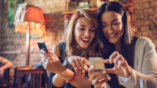 Happy women using their mobile phones while relaxing in a cafe.