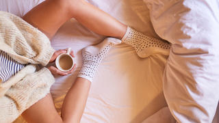 High angle shot of an unidentifiable woman drinking coffee while sitting on her bed