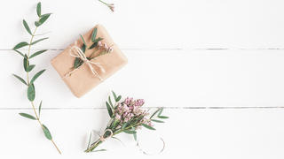 Flowers composition. Gift, pink flowers and eucalyptus branches on white wooden background. Flat lay, top view